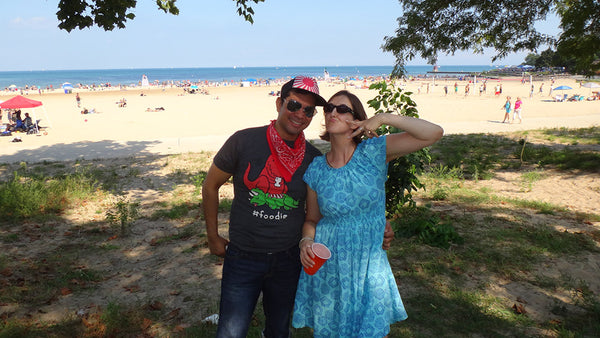 April wearing a short and patterned blue Mata dress next to her husband on a beach.