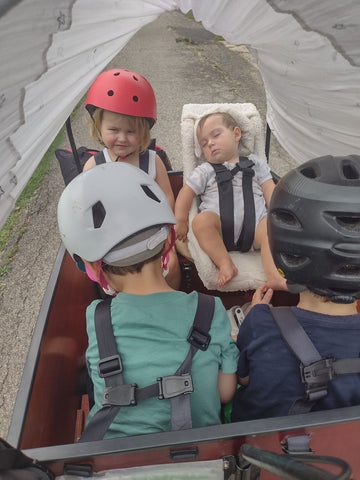 Three toddlers and a baby in the bunch bike with a sun shade.