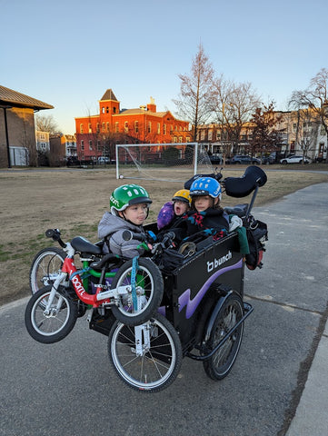 Three kids on a bunch bike with 2 woom bikes strapped to the front panel