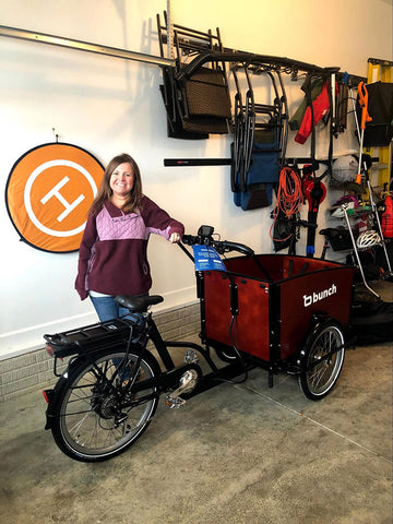 Woman smiling next to a new Bunch Bike family cargo bike in a garage. 