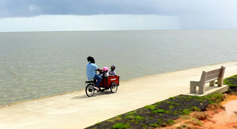 dad and kids ride cargo bike on beach path