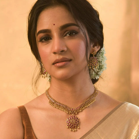 An image of a woman wearing a saree with an Indian style necklace with earrings