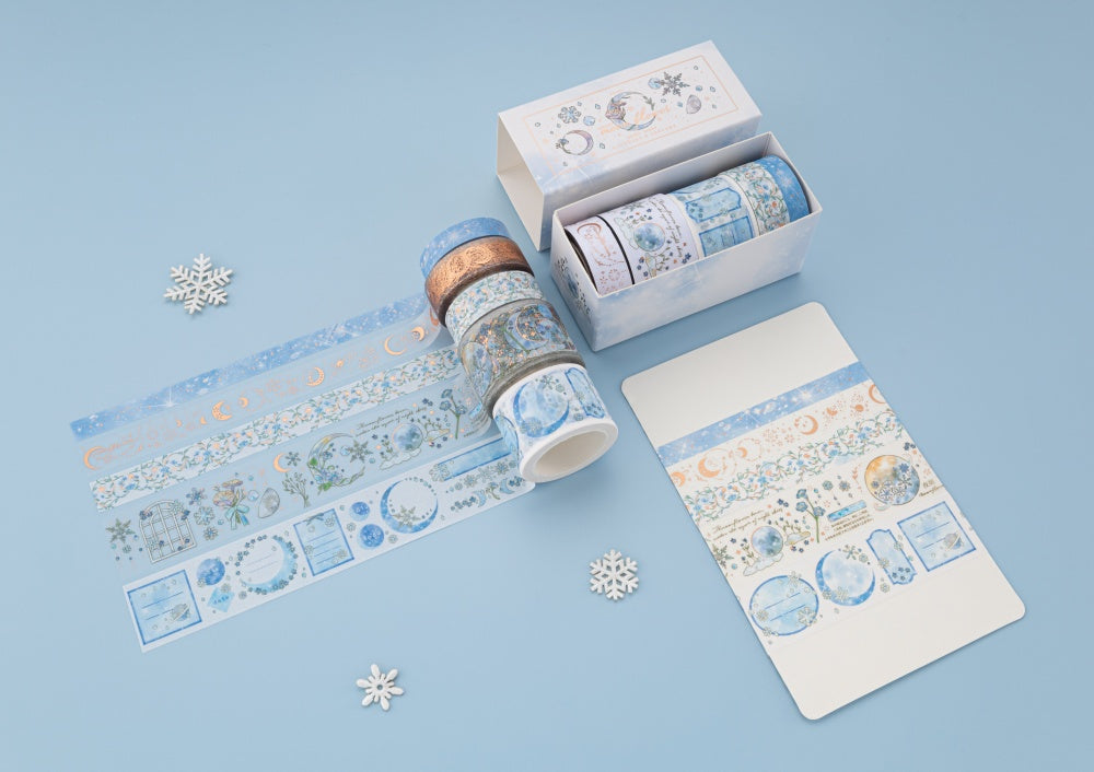 Flatlay of Winter Moonflower washi tapes with opened box and 5 washi tapes unrolled on blue background