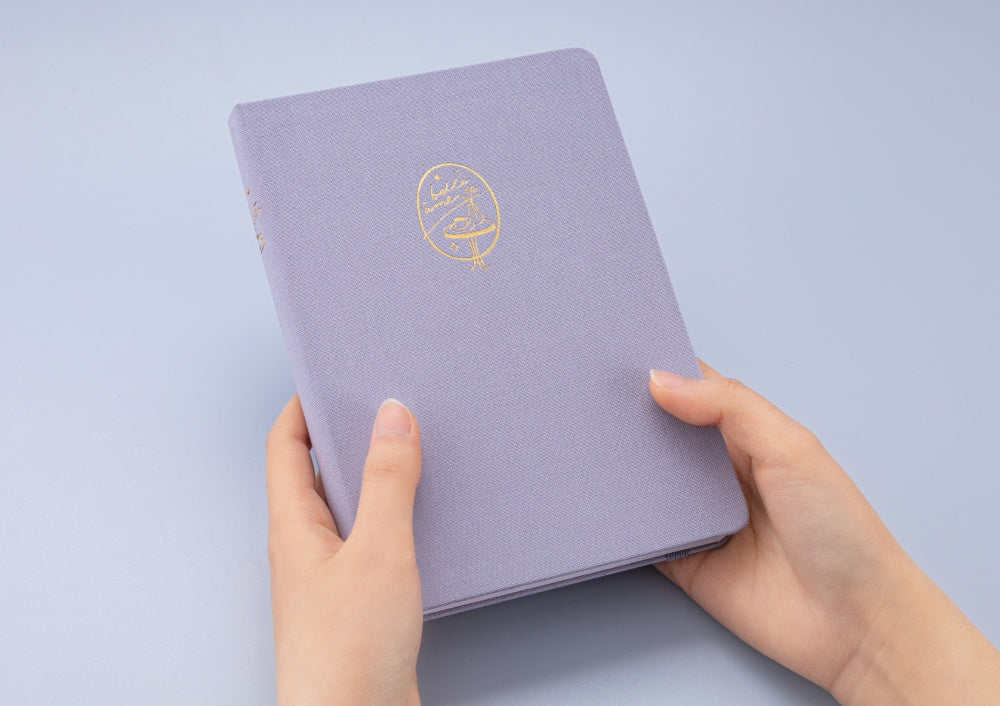 Hands holding Tsuki Love Lock bullet journal notebook at an angle to show gold edges