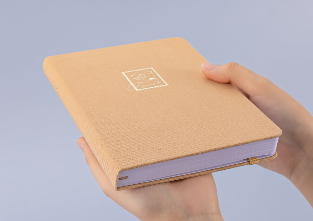 Hands holding Tsuki Love Lock bullet journal notebook at an angle to show gold edges