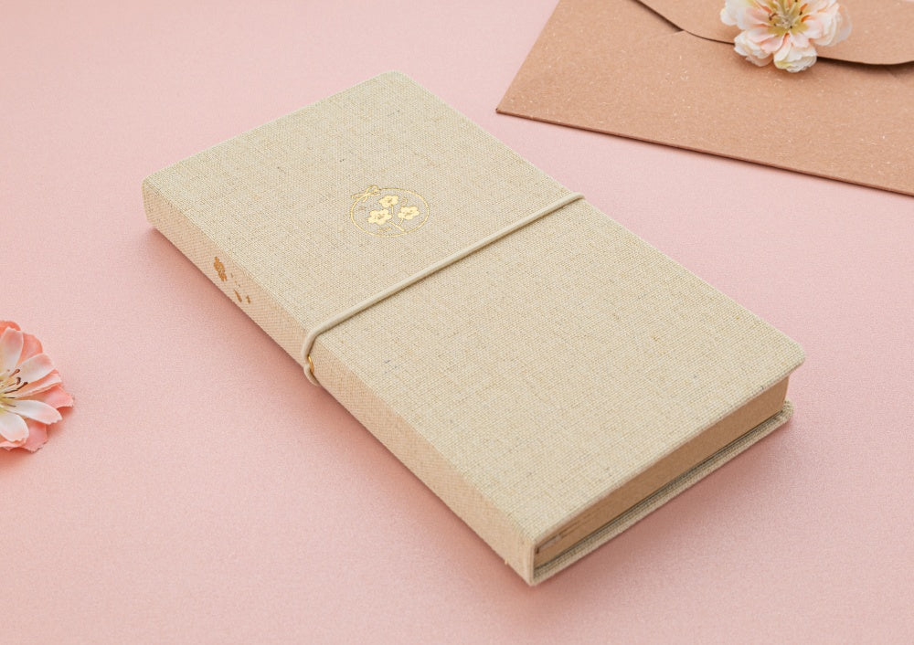 Tsuki ‘Sakura Breeze’ Kraft Paper Travel Notebook at an angle on pink background