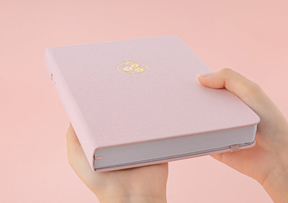 Hand holding Tsuki Sakura Breeze limited edition bullet journal by Notebook Therapy at an angle showing bottom part of notebook