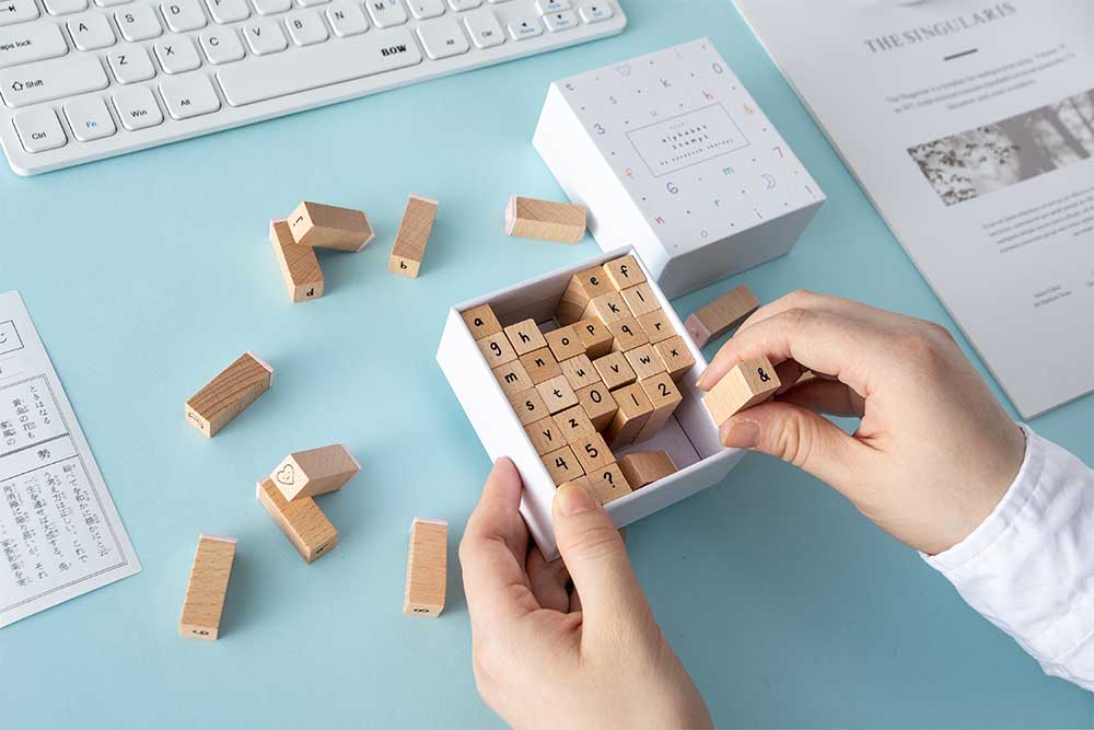 Wooden stamp being picked up from the box with the other wooden stamps scattered on the table