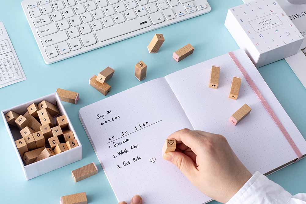 High-quality wooden stamps being used on a bullet journal for to-do lists. Text reads “To do list: 1. Exercise, 2. Walk Nori, 3. Get Boba”