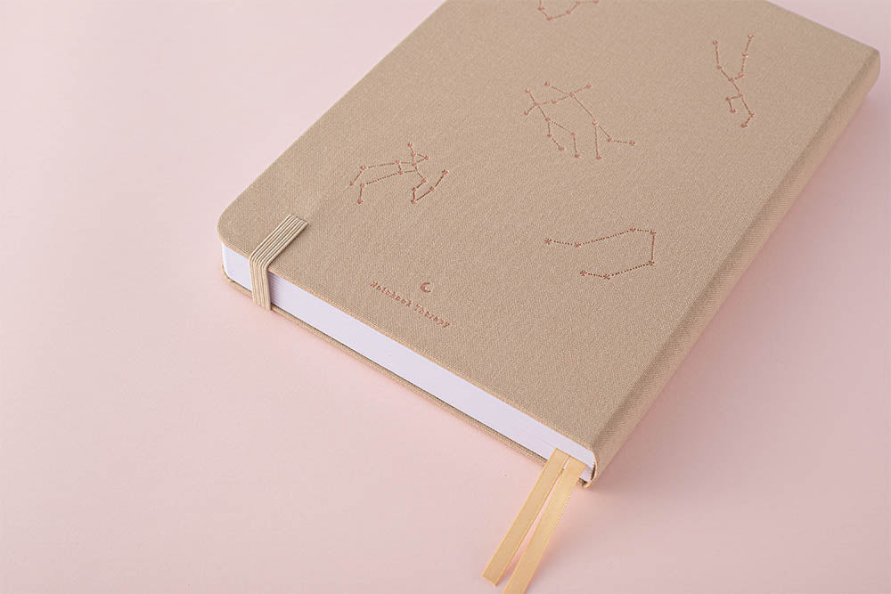 Beige constellation bullet journal back cover on a pink background