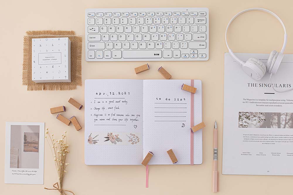 Tsuki Bullet Journal Typewriter Style Alphabet Stamps out of eco-friendly gift box packaging being used on open bullet journal with keyboard and headphones and paper on beige background