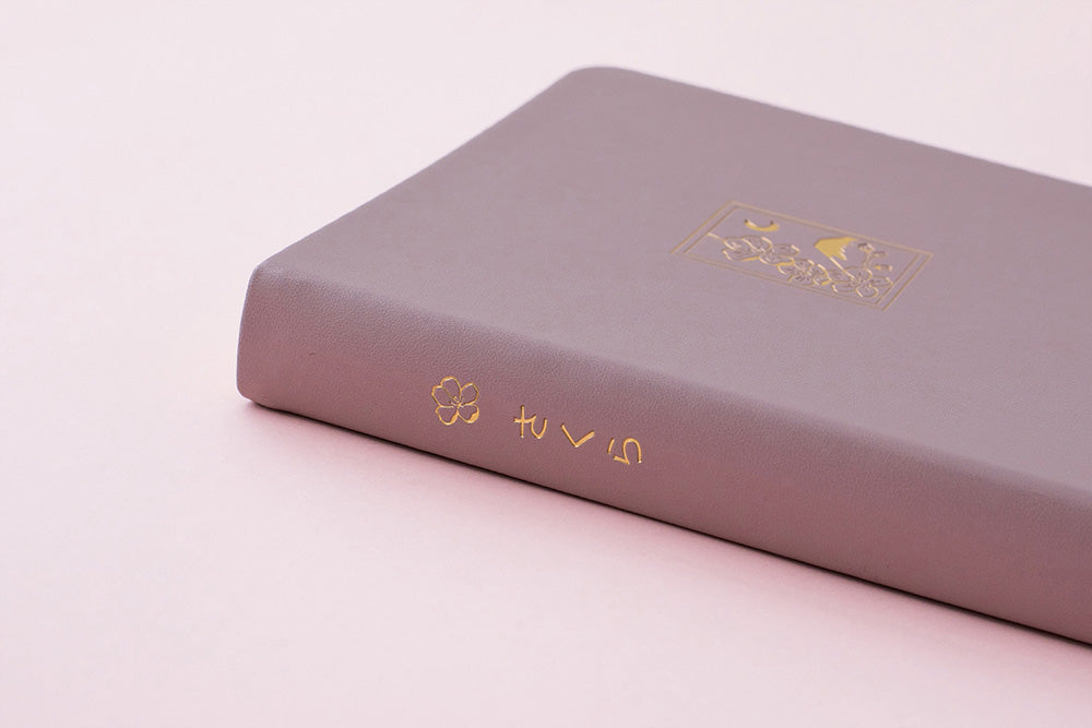 Side of blush pink bullet journal notebook with gold embellishments on a pink background