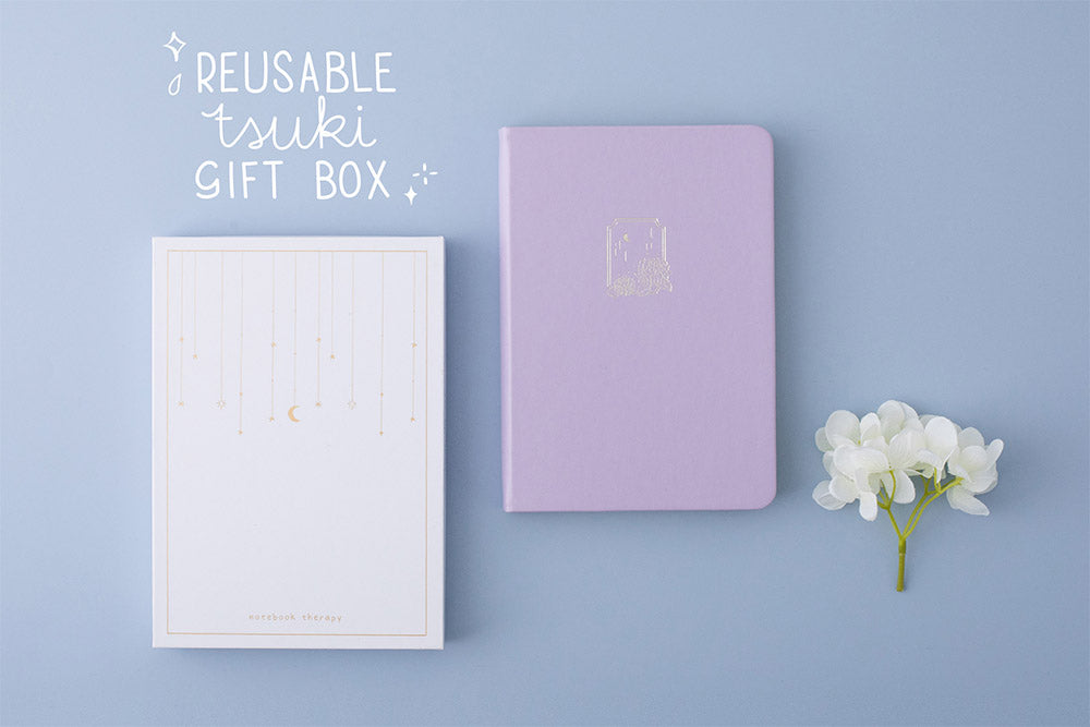 Tsuki Endless Summer Limited Edition Bullet Journal in Lilac Bloom with reusable Tsuki gift box and white hydrangea flowers on light blue background