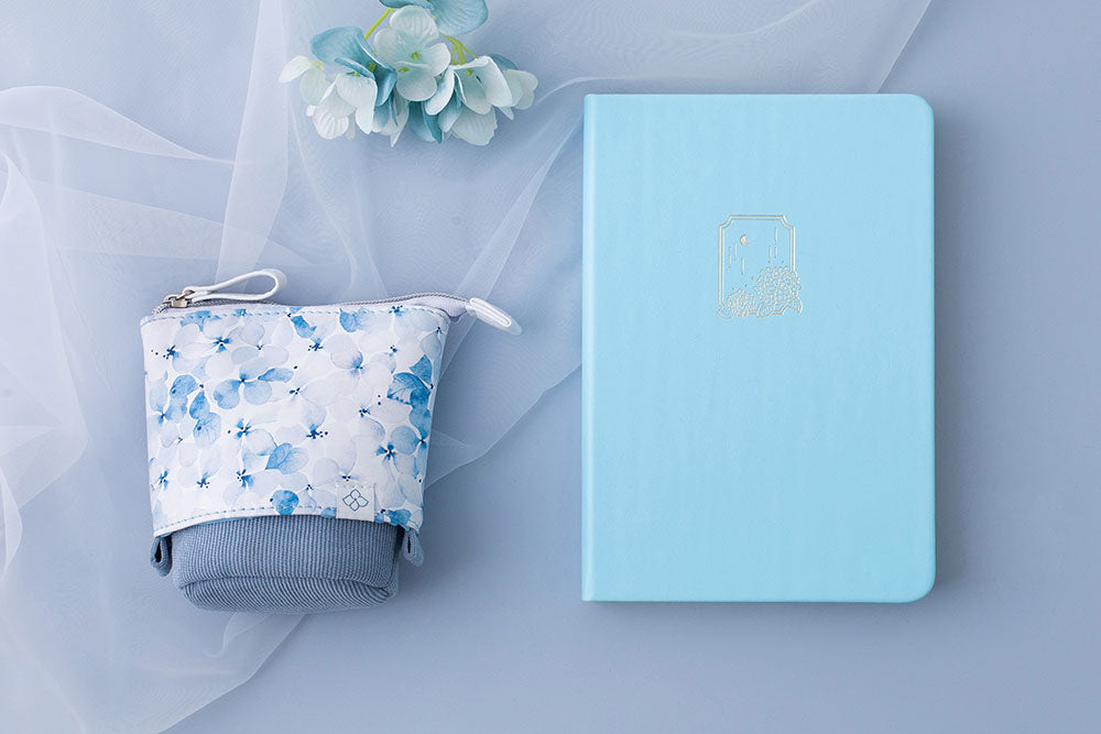 Tsuki Endless Summer Limited Edition Bullet Journal in Petal Blue with Tsuki Endless Summer Pop-Up Pencil case in light blue and light blue hydrangea flowers with netting on light blue background