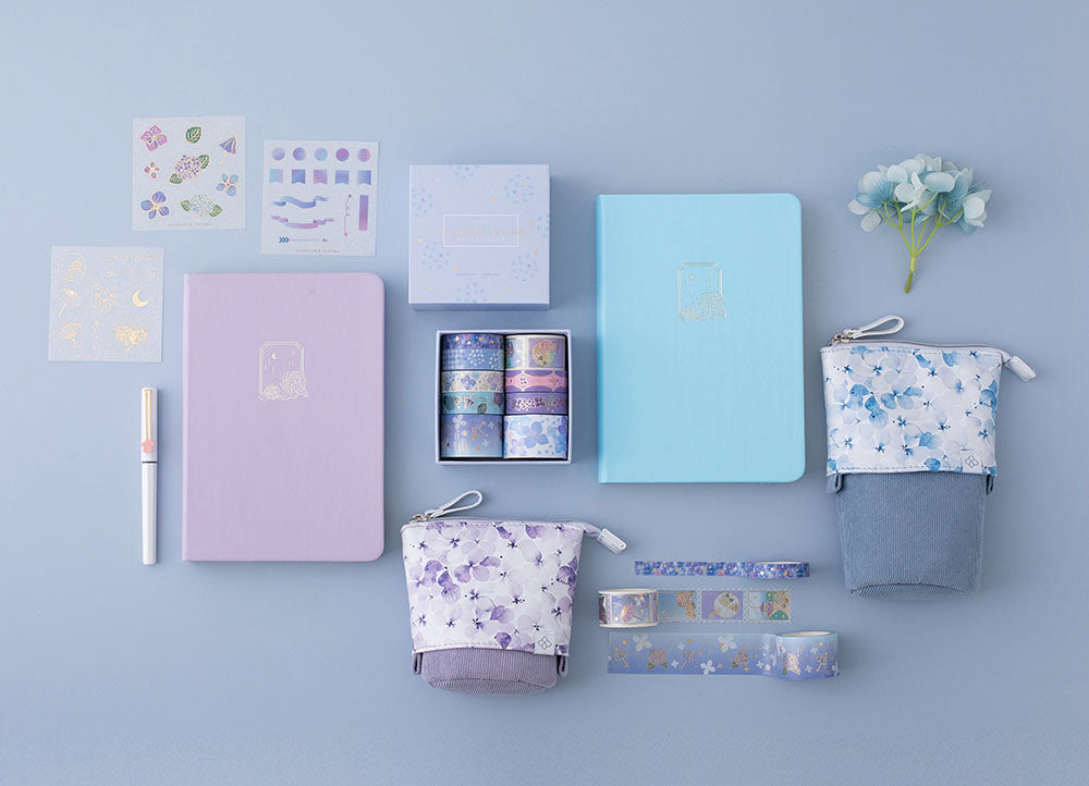 Tsuki Endless Summer Limited Edition Bullet Journals in Lilac Bloom and Petal Blue with Tsuki Endless Summer washi tape set and free sticker sheets with Tsuki Endless Summer Pop-Up Pencil cases with light blue hydrangea flowers and pen on light blue background