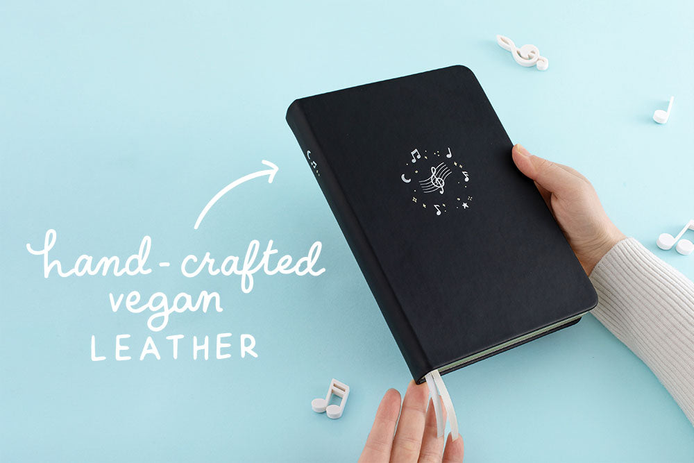 Tsuki Lunar Notes bullet journal in hands with hand-crafted vegan leather doodle images in blue background