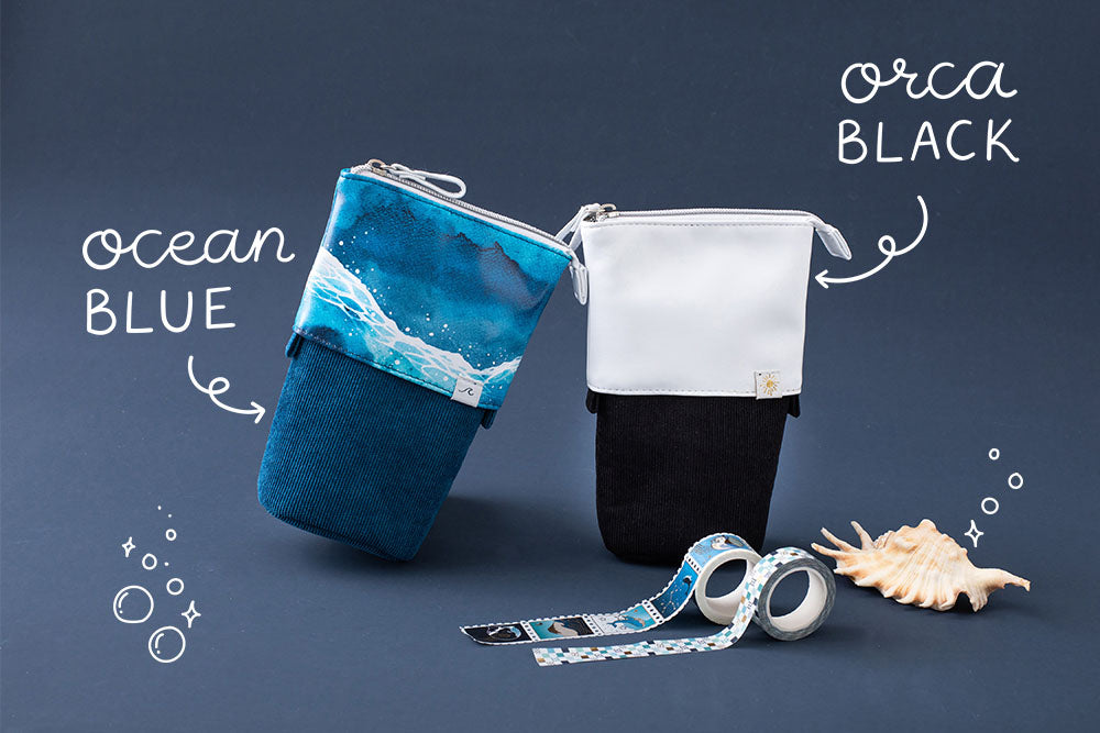 Tsuki Ocean Edition pop up standing pencil cases in Orca Black and Ocean Blue at an angle with Tsuki Ocean Washi Tape and seashell in dark blue background