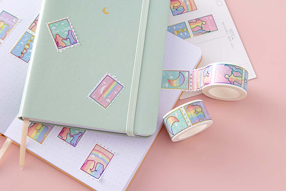 Close up of Tsuki Rainbow Pride Washi Tape on open notebook page with mint matcha Tsuki Pastel Edition Bullet Journal and postcard on light pink background