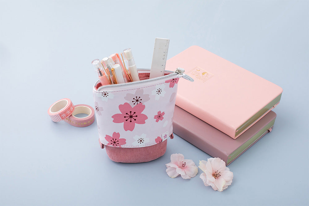 blush pink sakura pop up pencil case with petal pink and blush pink cherry blossom bullet journal notebook in blue background