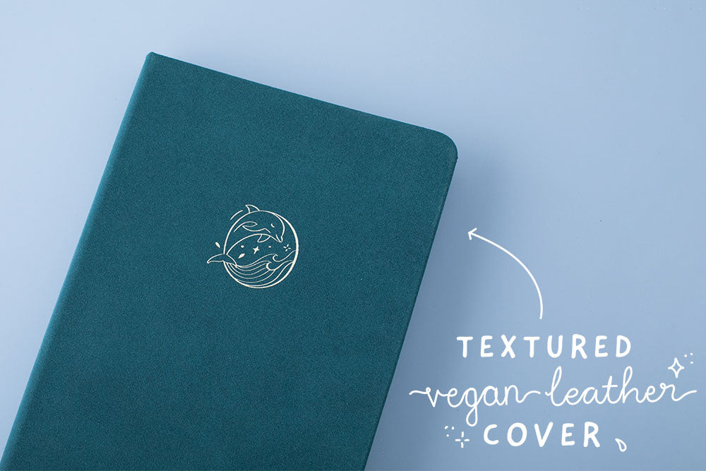 Close up of the front cover of Sea green textured vegan leather Tsuki Dolphin Days bullet journal on blue background