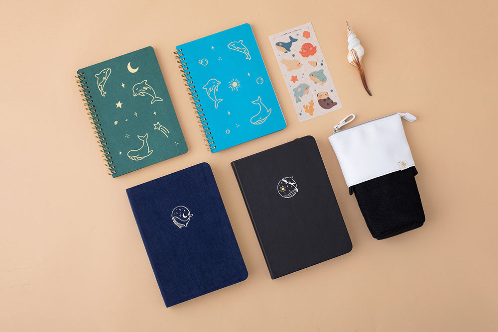 Tsuki deep black vegan leather Playful Orca limited edition notebook with seashell and aqua blue and moss green Ocean limited edition notebooks and deep blue Gentle Giant luxury edition bullet journal and Ocean pop up standing pencil case on peach background