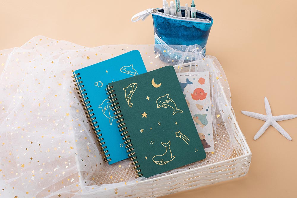 Tsuki Ocean Edition Ring Bound notebooks in aqua blue and deep teal with free sticker sheet and ocean edition pop up standing pencil case in ocean blue in basket with starfish in peach background
