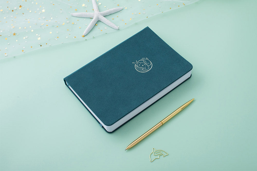 Tsuki sea green textured leather Dolphin Days notebook at an angle with starfish and gold pen and free dolphin gift on green background