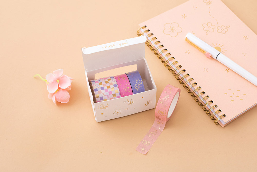 Tsuki Floral washi tapes in open box packaging with pink washi tape rolled out and honey peach ringbound bujo on peach background
