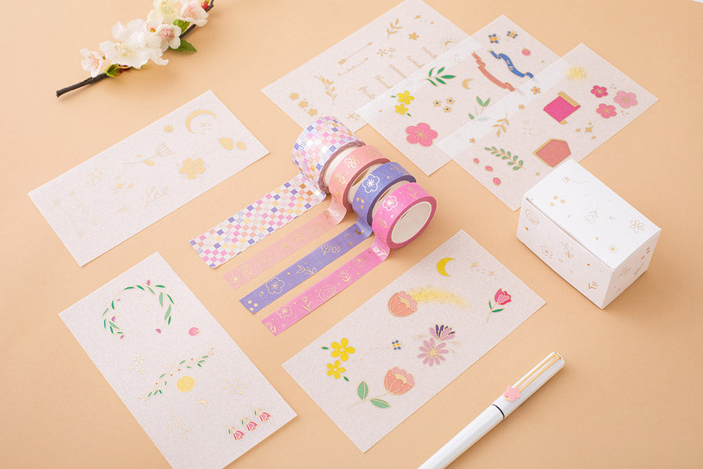 Tsuki Floral washi tapes rolled out with 6 sticker sheets laid out flat on a peach background