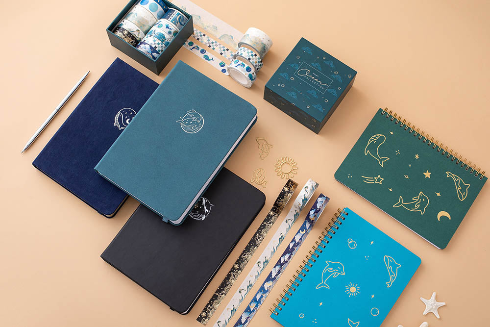 Ocean Collection washi tape with Tsuki sea green textured leather Dolphin Days notebook and Tsuki deep blue Gentle Giant notebook and Tsuki black Playful Orca notebook with two Ocean ring bound notebooks on peach background