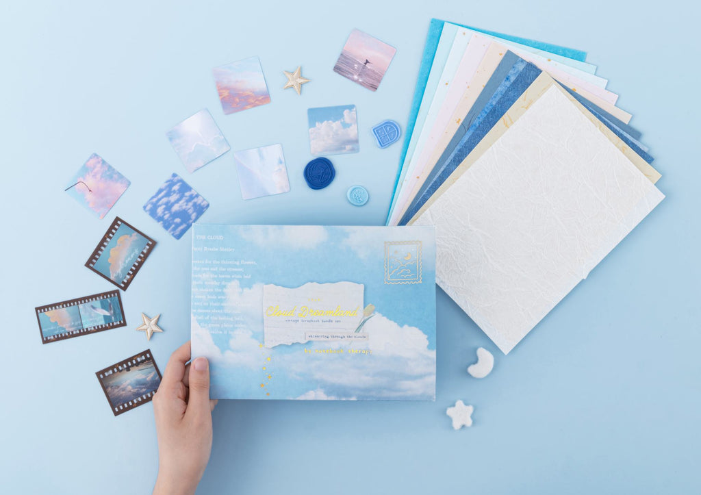 Hand holding the Cloud Dreamland scrapbook set box with the paper and stickers laid out in the background