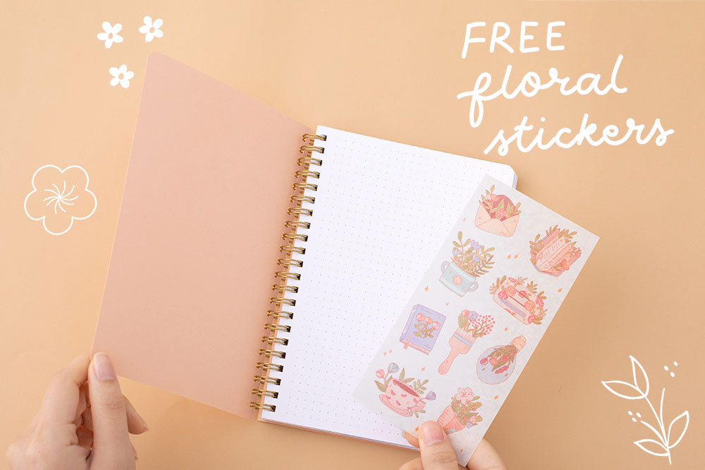 Tsuki Floral honey peach ringbound bujo open page with free sticker sheet held in hand on peach background