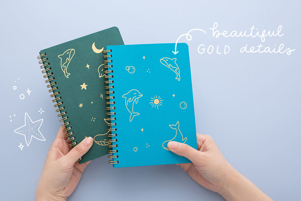 Tsuki Ocean Edition Ring Bound notebooks in aqua blue and deep teal with beautiful gold details held in hands in blue background