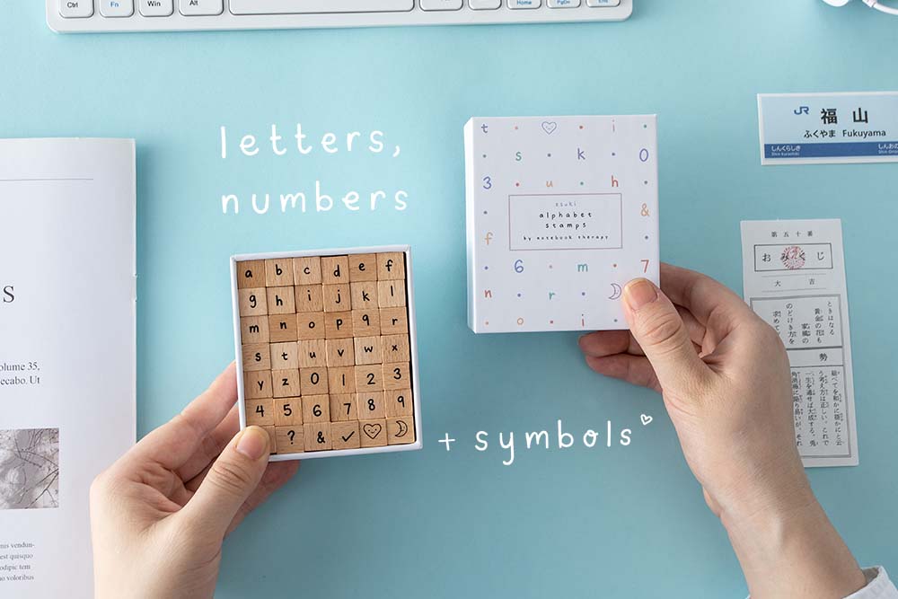 Alphabet Stamps by Notebook Therapy being shown against a blue background. Box open to show letters, numbers, and symbols included in the 42 Alphabet Stamp Set