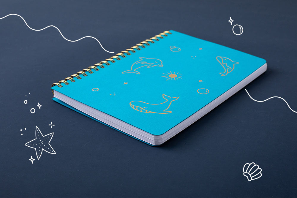 Tsuki Ocean Edition Ring Bound notebook in aqua blue at an angle on dark blue background