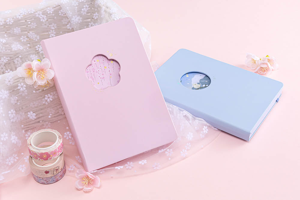 Tsuki Four Seasons: Spring Collector’s Edition 2022 Bullet Journal with Tsuki Four Seasons: Winter Collector’s Edition 2022 Bullet Journal and Tsuki ‘Sakura Journey’ Washi Tapes with sakura blooms on floral netting on basket on light pink background