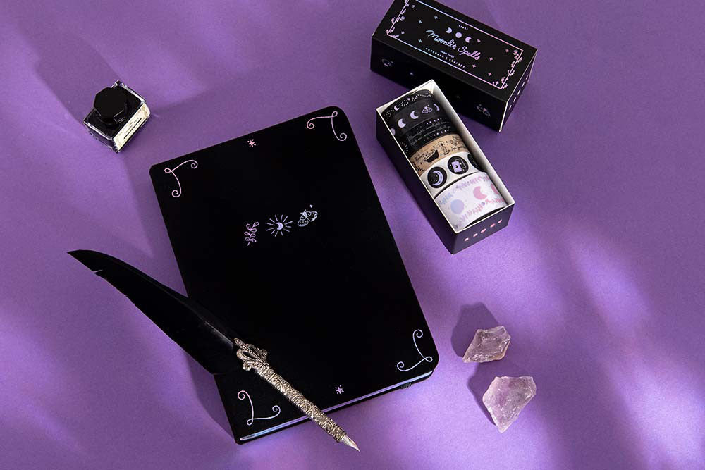 Tsuki ‘Moonlit Spell’ Limited Edition Holographic Bullet Journal with Tsuki ‘Moonlit Spell’ Washi Tape Set with black ink and black feather quill and amethyst stones on purple background