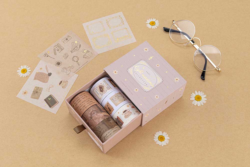 Tsuki Light Academia Washi Tape Set by Notebook Therapy on brown background with a pair of glasses and some pressed daisies around the open box