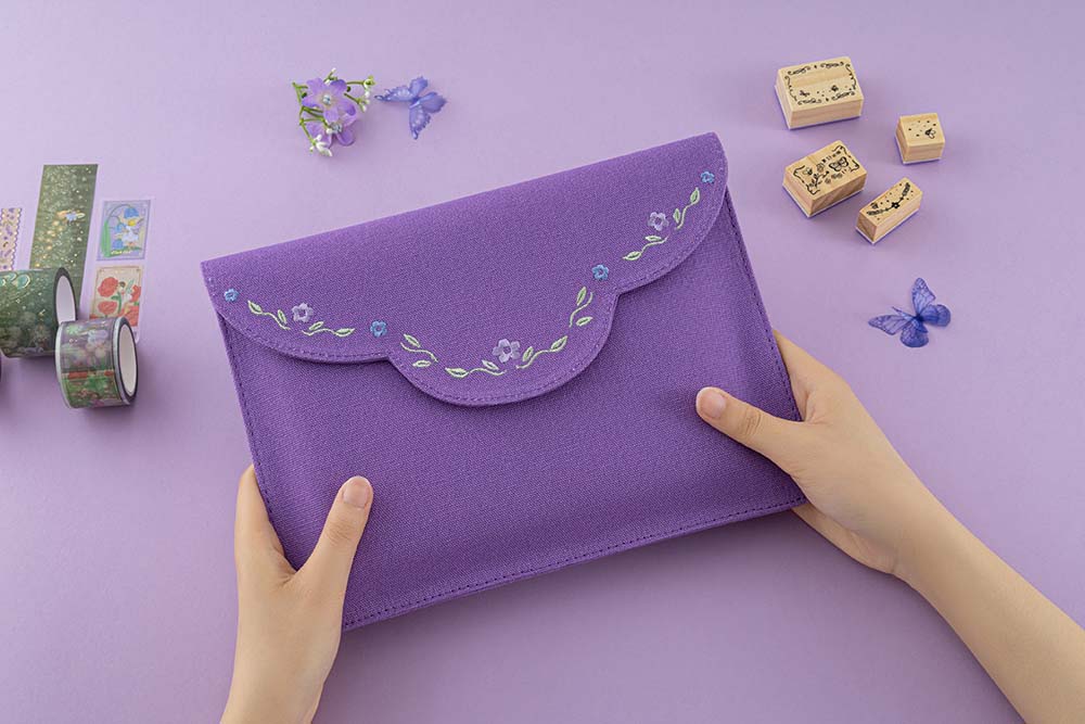 Hands holding a purple notebook pouch with embroidered details