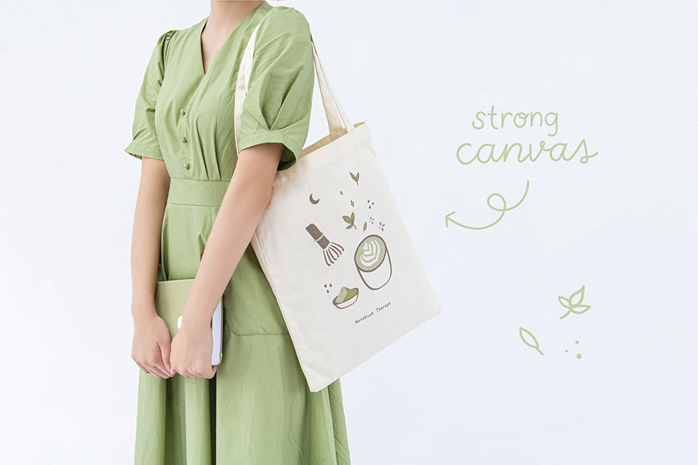 Tsuki ‘Matcha Matcha’ Tote Bag with strong canvas on model’s arm with Tsuki ‘Matcha Matcha’ Limited Edition Bullet Journal held in arms in light grey background