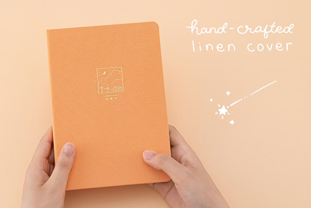 Hands holding the Tsuki Golden Hour Bullet Journal Box Set bullet journal notebook with orange background