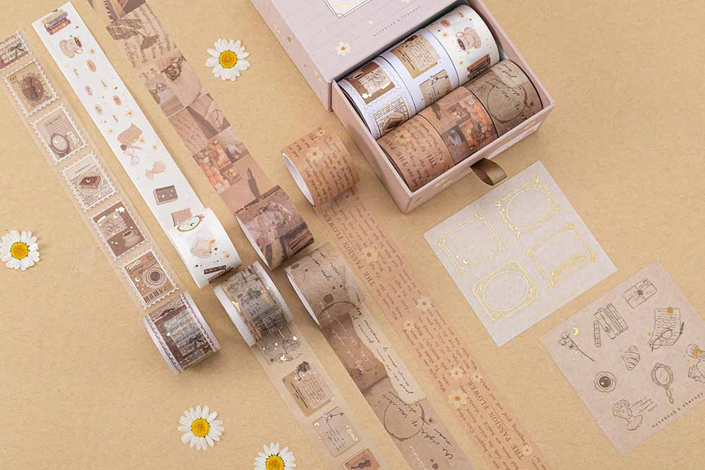 Tsuki Light Academia Washi Tape Set by Notebook Therapy on brown background with a pair of glasses and some pressed daisies around the open box and washi tape rolls