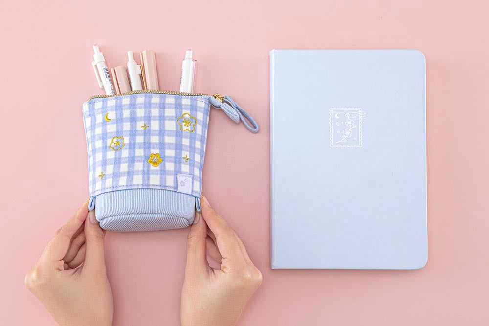 Tsuki ‘Sakura Journey’ Pop-Up Pencil Case with pens inside held in hands with Tsuki ‘Sakura Journey’ Limited Edition Bullet Journal on light pink background