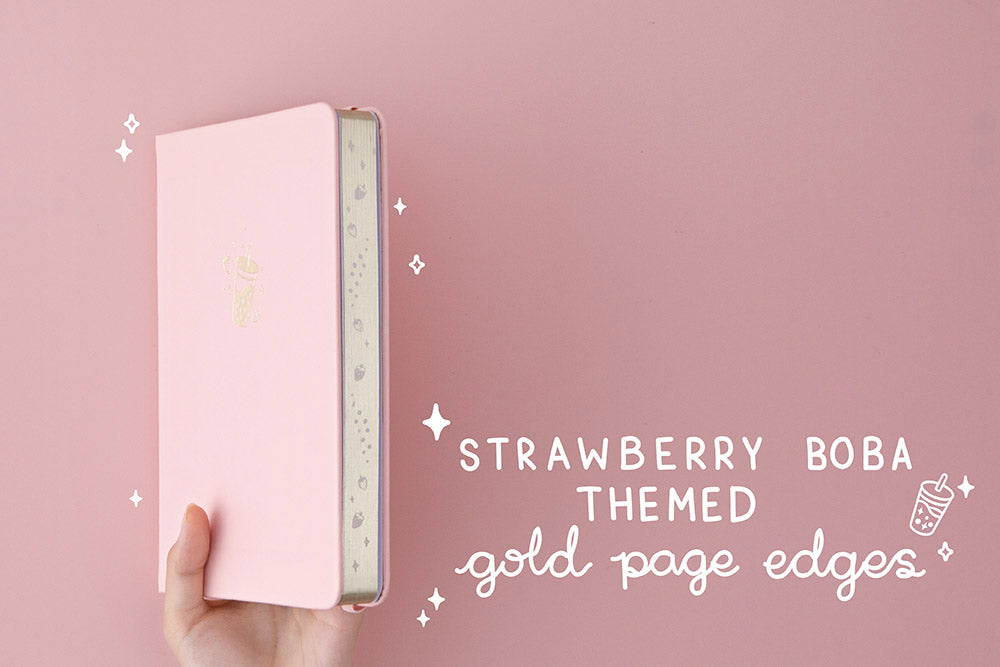 suki ‘Ichigo’ Limited Edition Boba Bullet Journal with strawberry boba themed gold page edges held in hands at an angle in light pink background