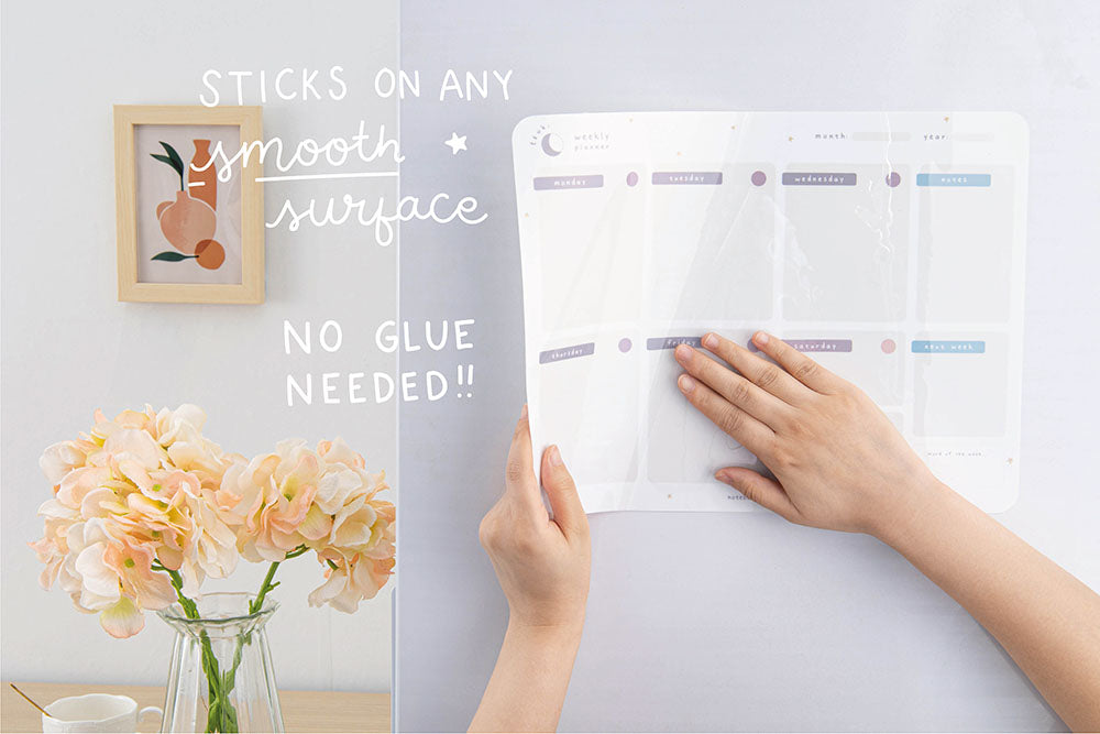 Tsuki Reusable Weekly Planner with no glue needed that sticks onto any smooth surface held in hands on fridge surface with flowers and framed image and mug