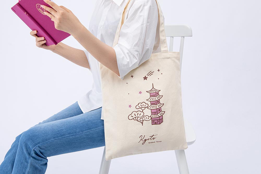 A figure carrying a Kyoto tote bag and a pink notebook