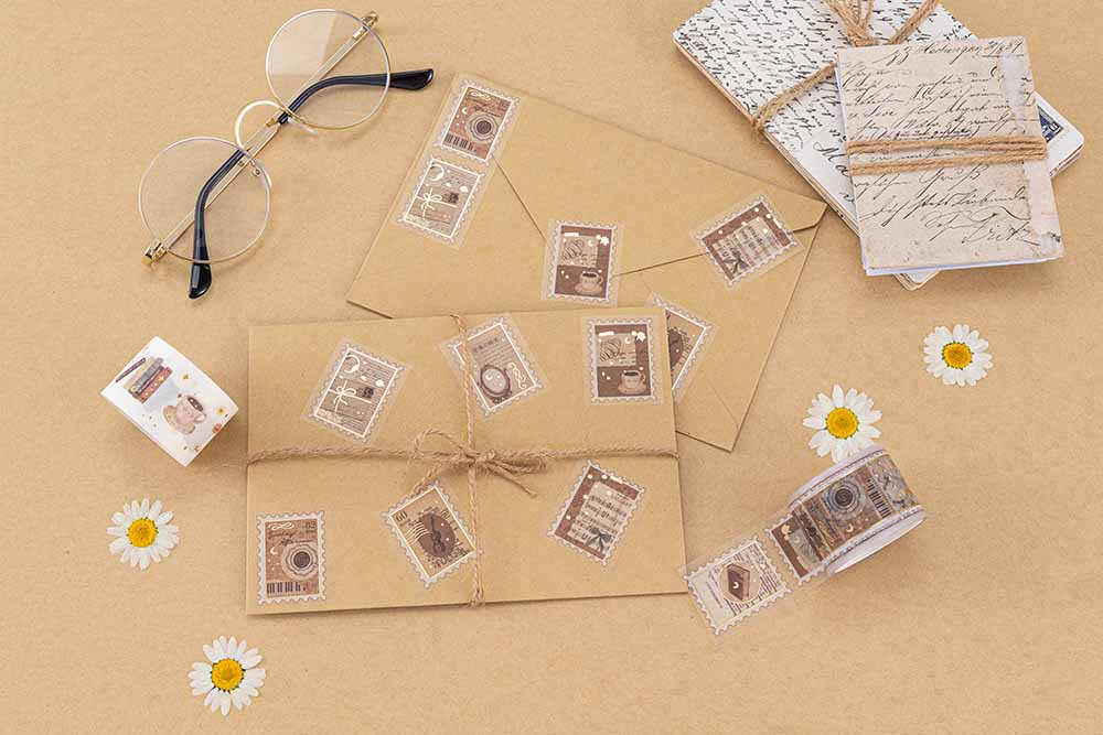 Tsuki Light Academia Washi Tape stamp roll cut up and stuck on brown envelopes with text ‘vintage aesthetic’ written in white, a pair of glasses and pressed daisies around the subject
