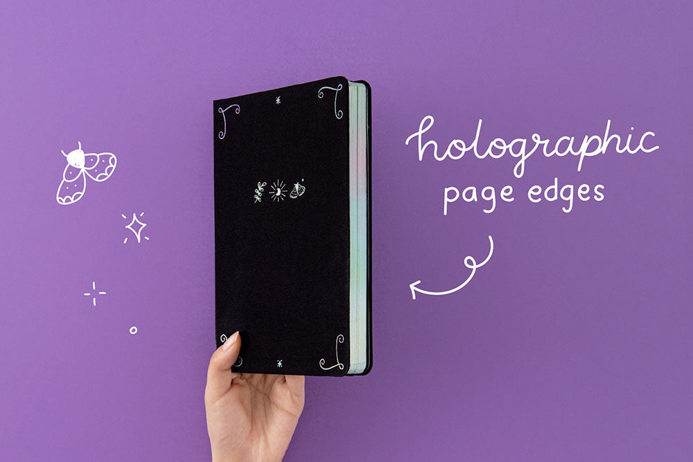 Tsuki ‘Moonlit Spell’ Limited Edition Holographic Bullet Journal with holographic page edges held in hand in purple background