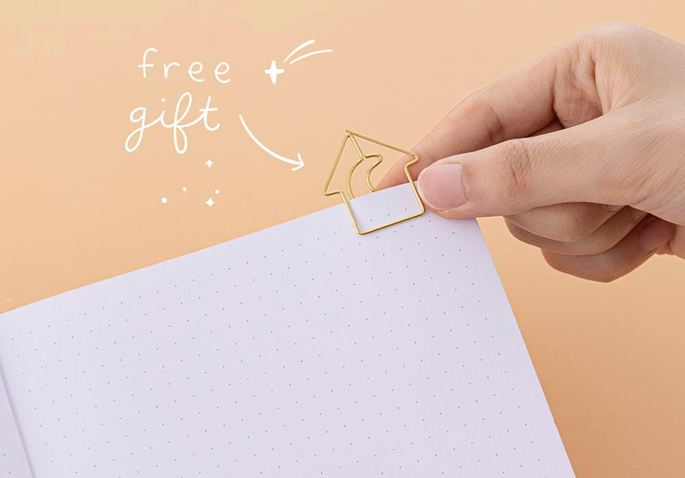 Hand holding Tsuki Golden Hour Bullet Journal notebook free gift which is a gold house shaped paperclip with a crescent moon in the middle