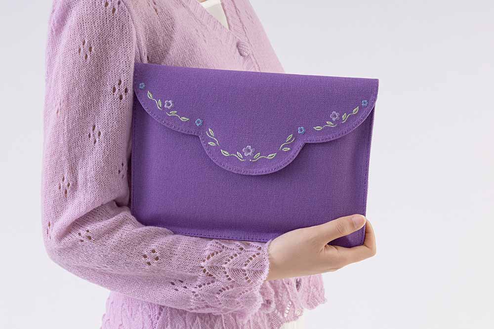 Person wearing lilac knitted jumper carrying the purple notebook pouch showing front design